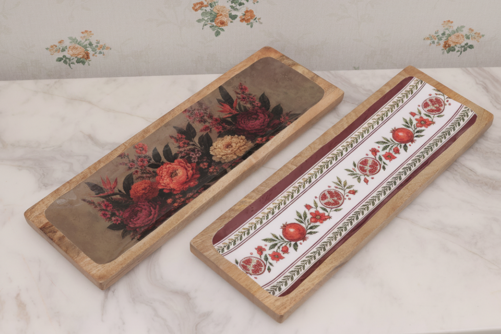 Two rectangular decorative trays with wooden edges, displayed on a white marble surface against a floral wallpaper background. One tray features a dark floral design, and the other has a white background with red floral motifs and green borders.